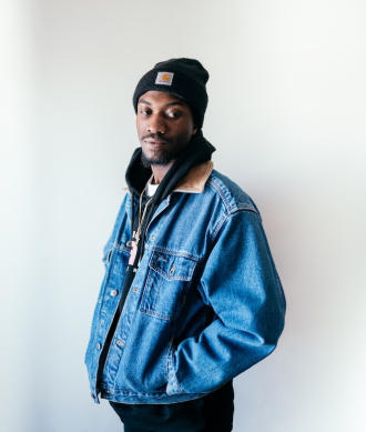 Homem negro de toca preta com a jaqueta jeans e as mãos no bolso